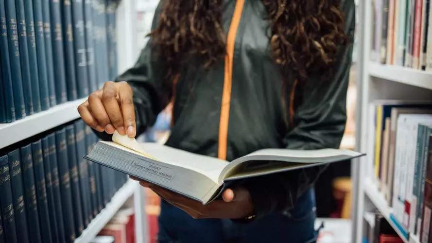 student holding a large book in a library corridor at Lincoln College
